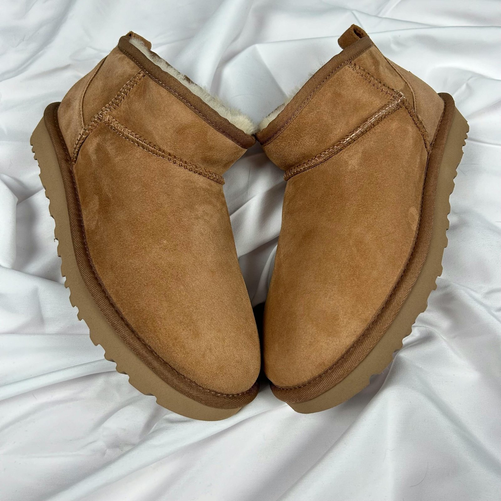  pair of new brown suede boots with fur lining, placed on a white fabric background.